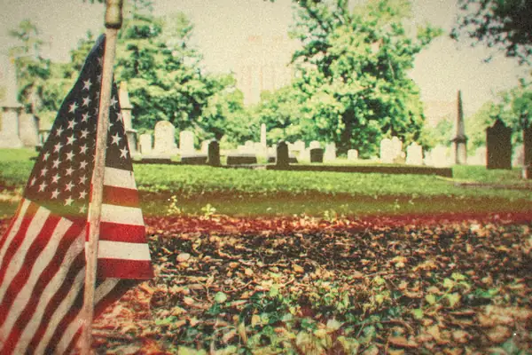 A small American flag planted in the grass of a quiet cemetery.