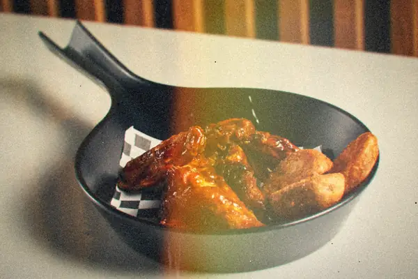 Barbecue-glazed chicken wings with crispy potato wedges in a black skillet.