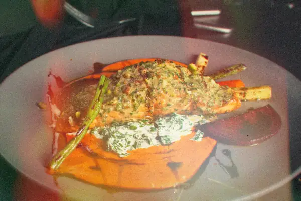 A salmon fillet with a green herb topping on a plate with roasted vegetables, beets and creamed spinach.