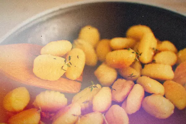 Golden pan-crisped gnocchi with thyme being turned with a wooden spatula.