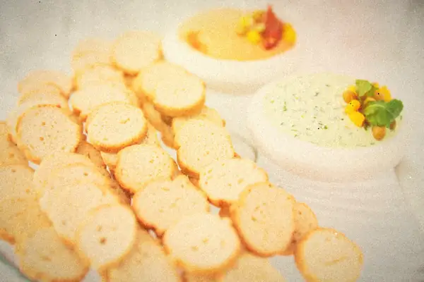 A bowl of creamy green spinach dip beside a pile of toasted baguette crisps.