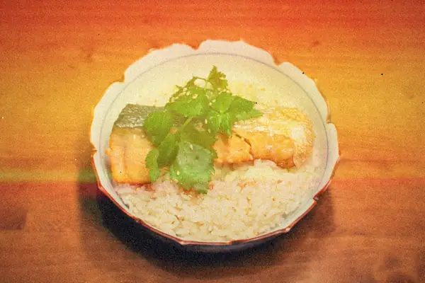 A bowl of white rice topped with glazed salmon, sesame seeds and fresh cilantro.