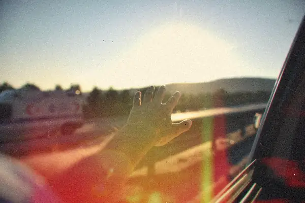 A hand reaching out a car window toward the setting sun.