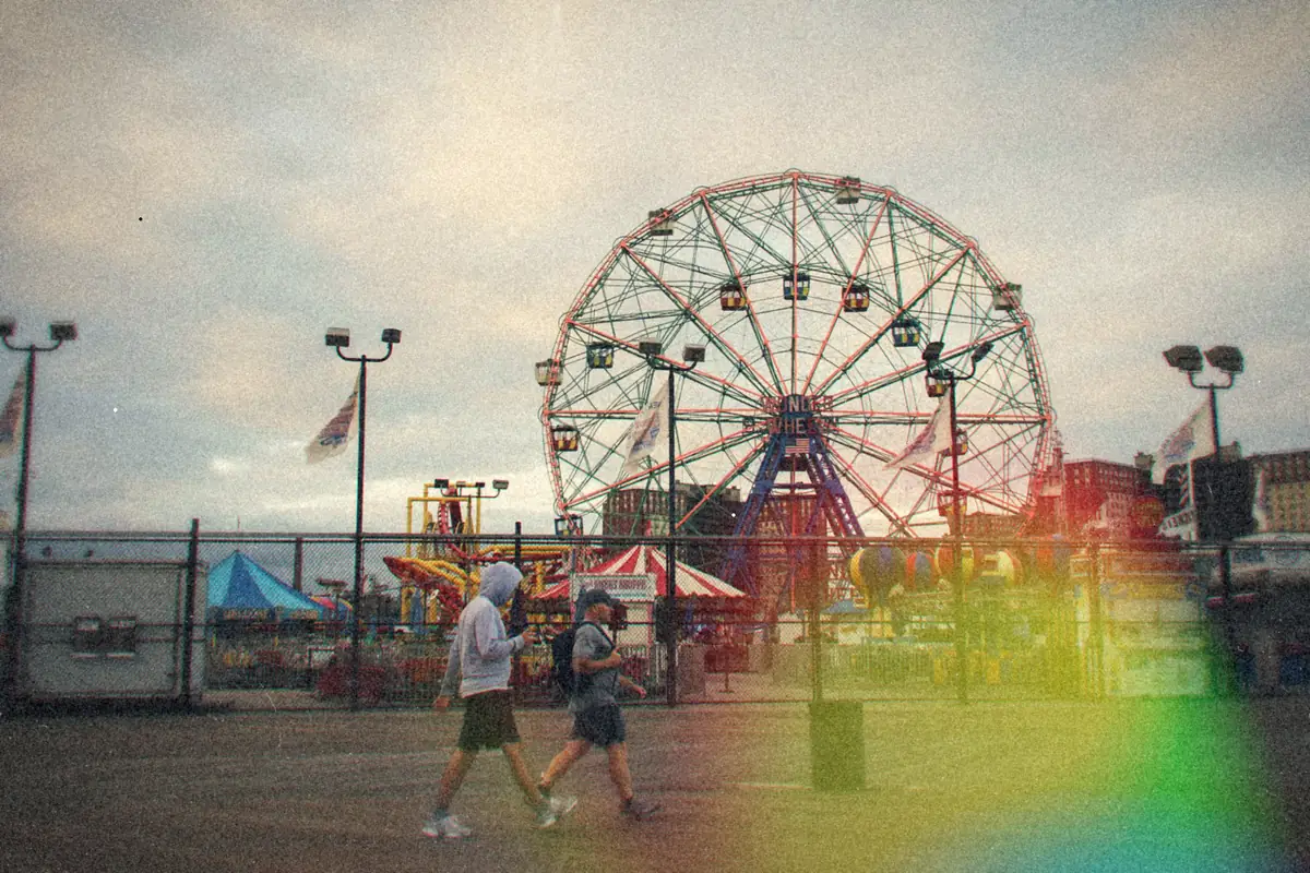 Two people walking the Coney Island boardwalk past the Wonder Wheel on a gray morning.