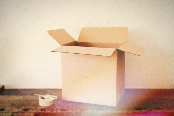 An open cardboard box on an old wooden desk next to a roll of tape.