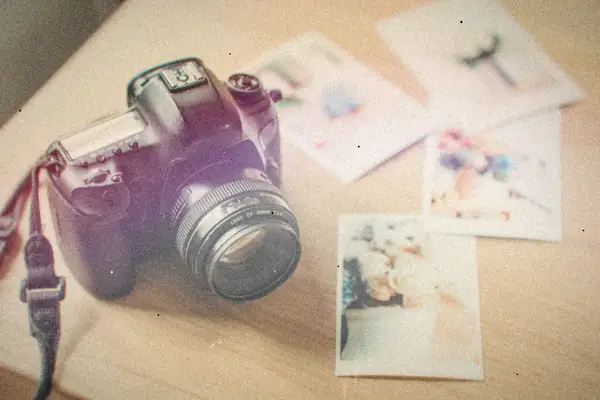 A DSLR camera resting on a wooden table beside a scatter of printed photos.