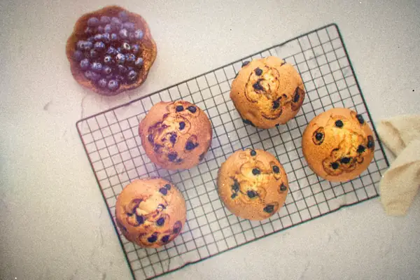 Six blueberry muffins cooling on a wire rack next to a small bowl of fresh blueberries.