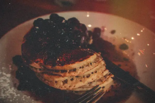 A stack of pancakes topped with blueberries and syrup on a white plate.