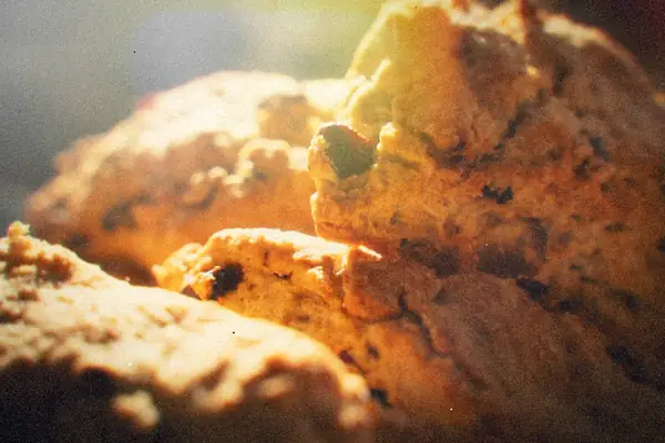 A close-up of rustic, craggy scones studded with dried fruit in warm light.