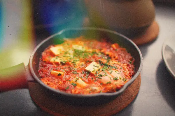 A small cast-iron skillet of a chunky red tomato and pepper stew sprinkled with chopped herbs.