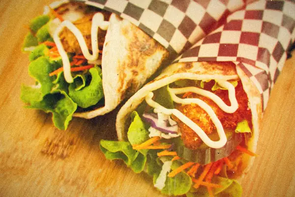 Crispy chicken wraps with lettuce, cucumber, shredded carrot and a creamy drizzle in checkered paper.