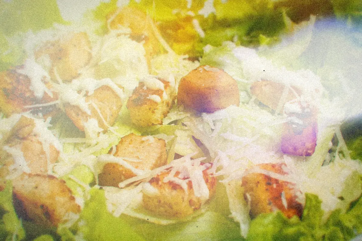 A close-up of Caesar salad with grilled chicken pieces, croutons, shaved Parmesan and creamy dressing.