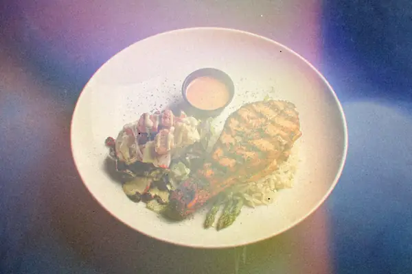 A spice-crusted grilled salmon fillet with rice, asparagus and a dipping sauce on a white plate.