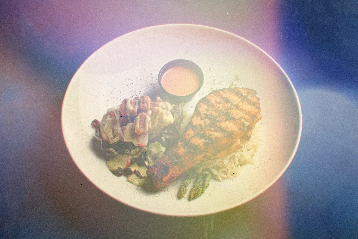 A spice-crusted grilled salmon fillet with rice, asparagus and a dipping sauce on a white plate.