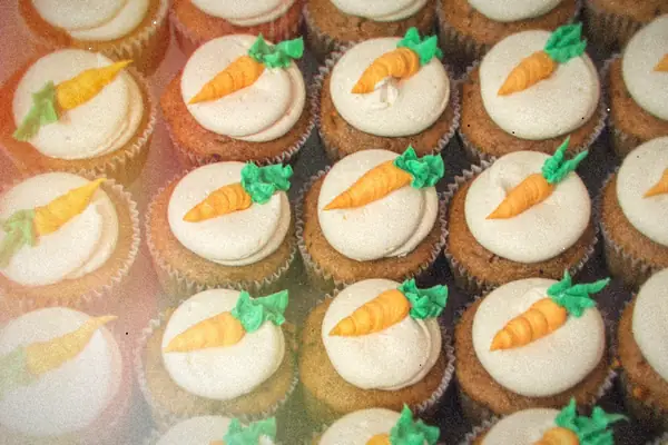 Rows of carrot cake cupcakes with cream cheese frosting and little piped carrots.