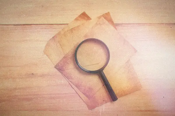 A magnifying glass resting on a few sheets of aged paper on a wooden table.