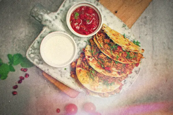 Quesadillas stuffed with seasoned ground meat and herbs on a marble board, with salsa and a creamy dip.