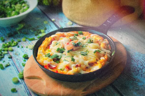 A cast-iron skillet of baked eggs with melted cheese, tomato pieces and green onions on a wooden board.
