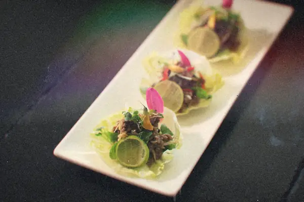 Three lettuce cups filled with seasoned meat, herbs and lime slices on a white platter.