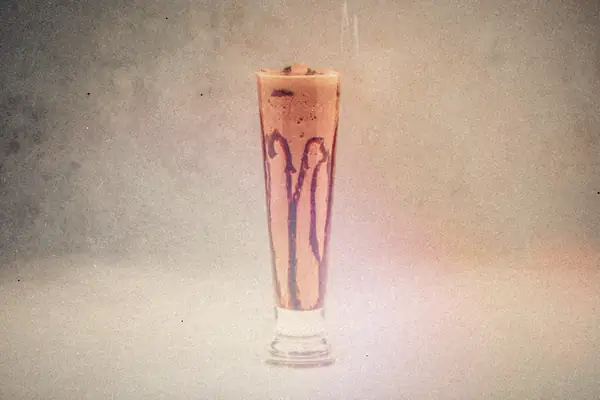 A chocolate shake with chocolate drizzle inside a tall glass on a gray background.
