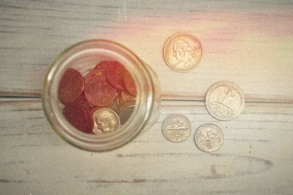 A glass jar full of coins on a wooden table.