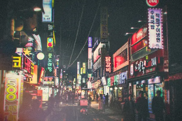 People walking down a neon-lit street at night in Seoul.