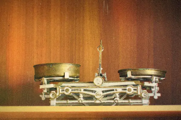 A vintage brass balance scale with two pans sitting on a wooden shelf.