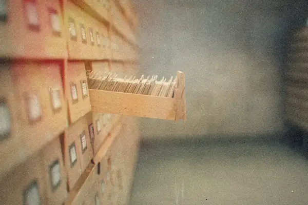 A drawer of index cards pulled out from a wall of wooden card catalog drawers.