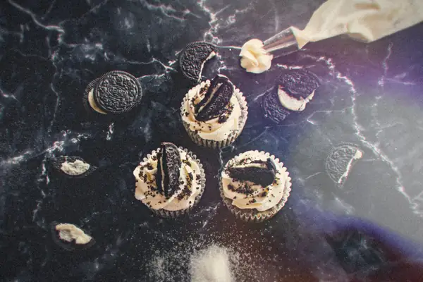 Cookies and cream cupcakes topped with frosting and chocolate sandwich cookies on a dark marble counter.