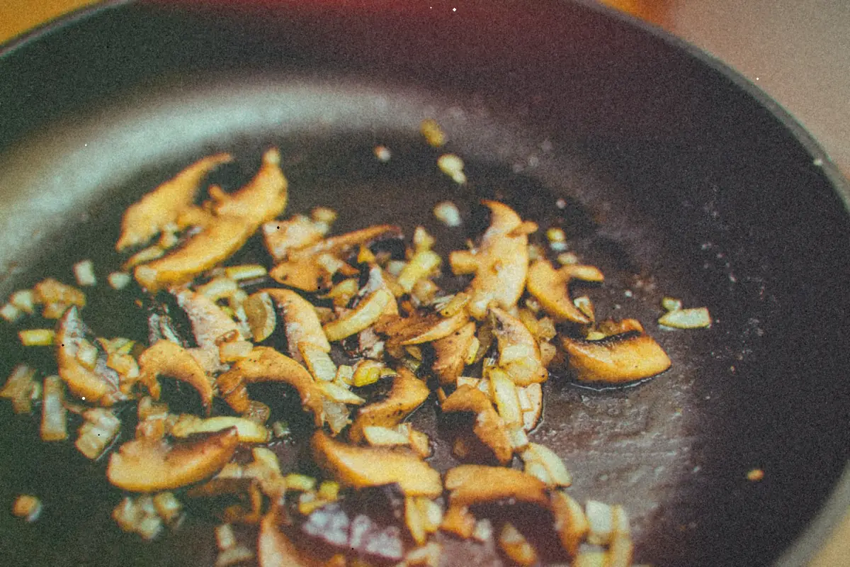 Sliced mushrooms and chopped onions sauteing in a dark skillet.