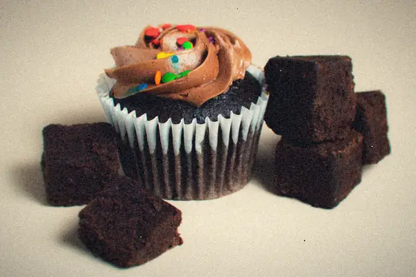 Fudgy brownie squares around a chocolate cupcake with chocolate frosting and colorful candy sprinkles.