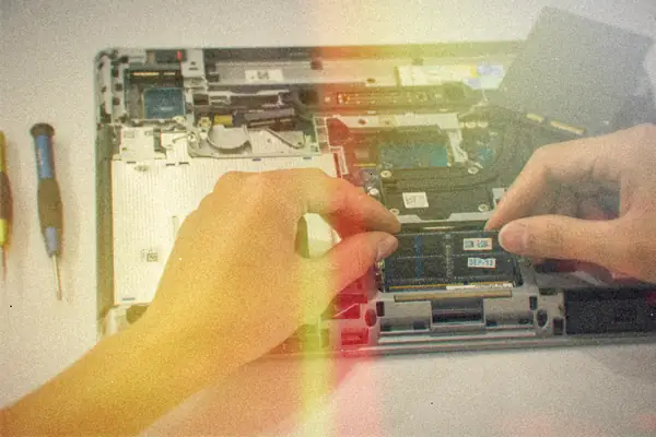 Hands working inside an opened business laptop with its 2.5-inch drive lifted out beside two screwdrivers.