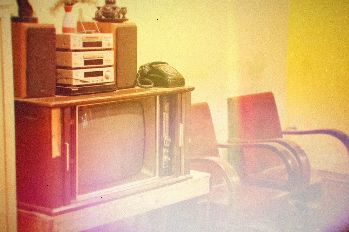 An old wood-cabinet television and stereo in a warmly lit living room with wooden chairs.