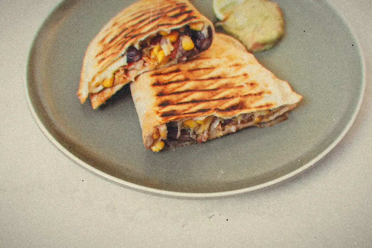 A grill-marked folded tortilla wrap cut in half, stuffed with beans, corn and cheese, with a green sauce.