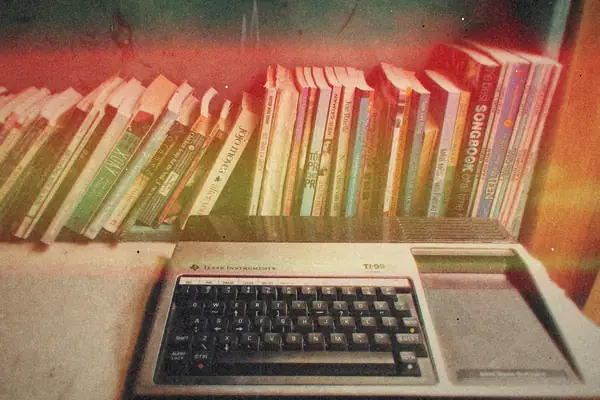 A beige vintage home computer keyboard sitting in front of a crowded bookshelf.