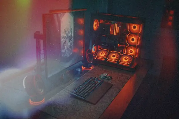A gaming PC with glowing orange case fans beside a monitor and keyboard on a dark desk.