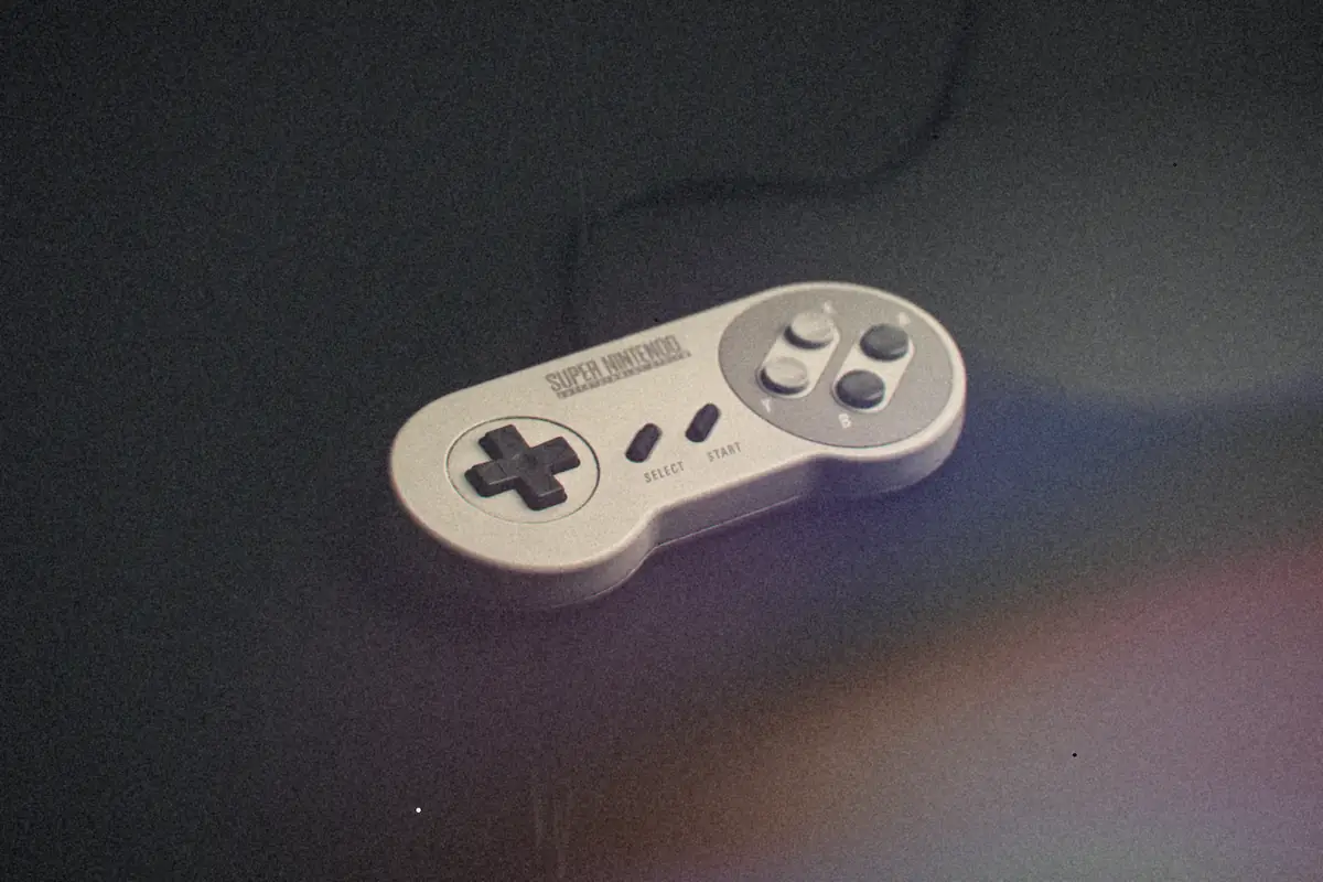 A grey Super Nintendo-style controller with a black d-pad lying on a black surface, cord curling away behind it.