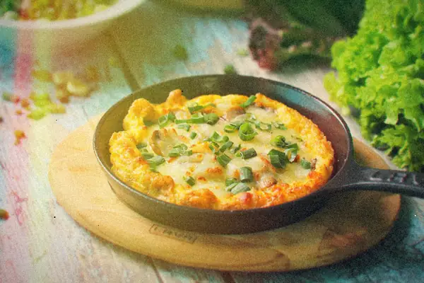 A cheesy omelet topped with green onions in a cast iron skillet on a rustic table.