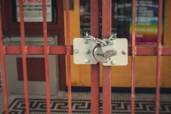 A heavy padlock and chain holding a red metal security gate shut.