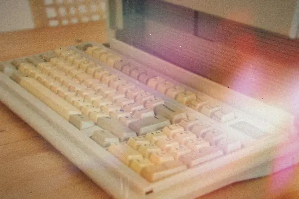 A vintage computer keyboard with yellowed keys on a wooden desk.