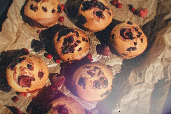 Berry muffins with raspberries and currants scattered on crumpled baking paper.
