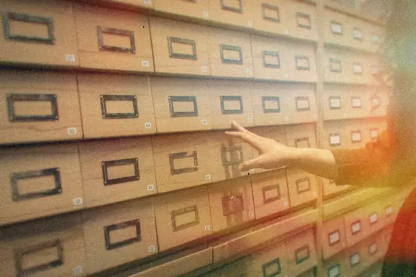 A hand reaching for one of many labeled wooden drawers in an archive room.