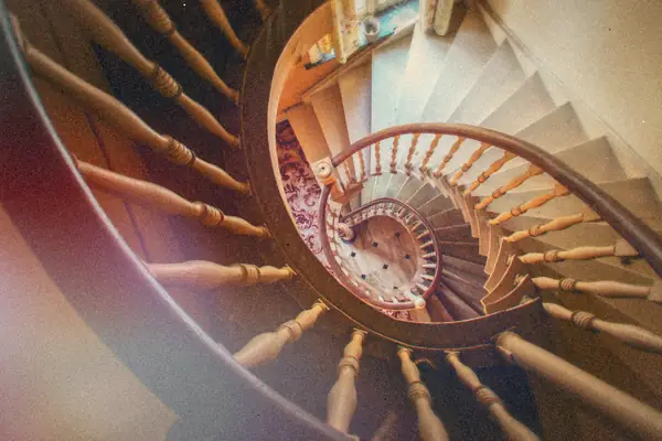 Looking down a wooden spiral staircase that curls around and around in an old house.