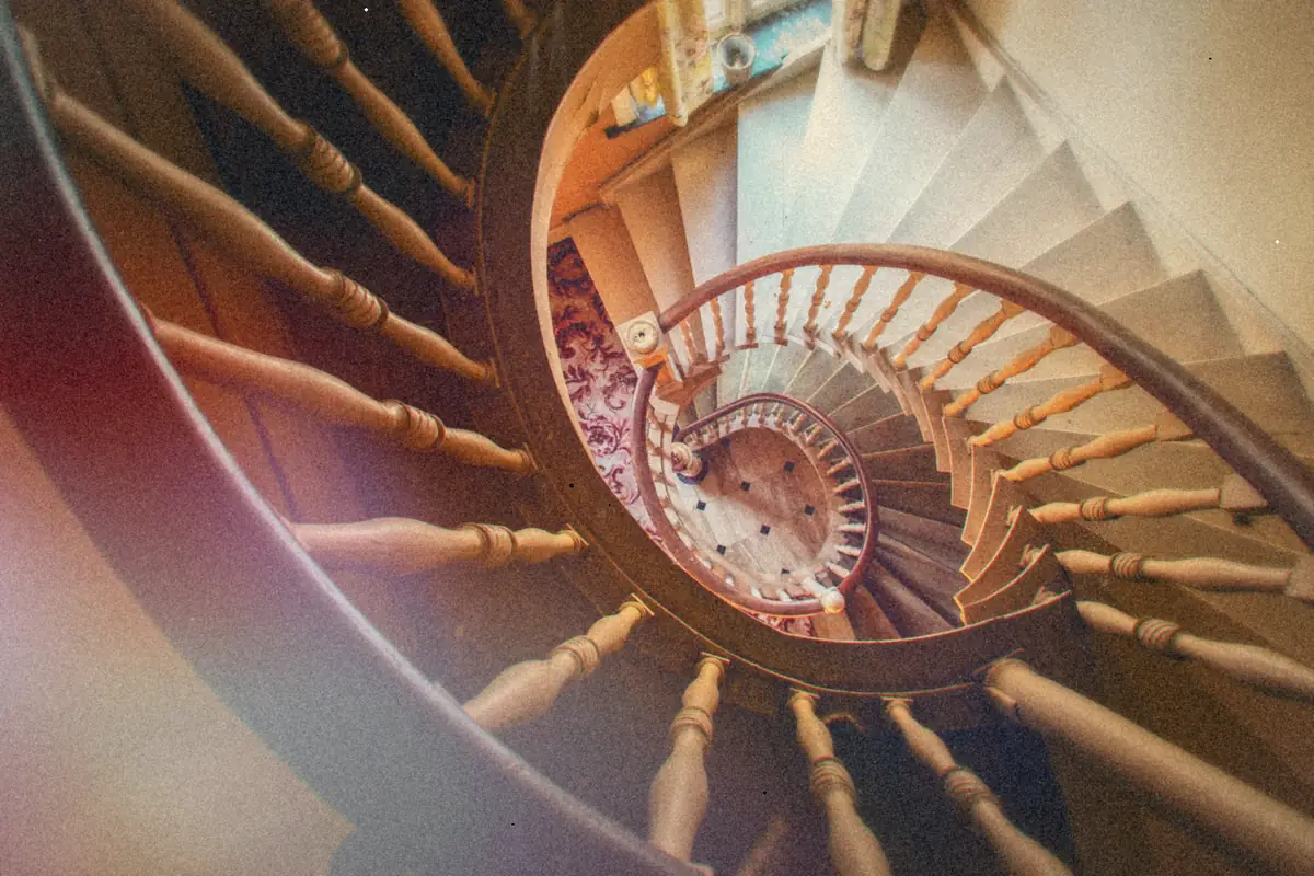 Looking down a wooden spiral staircase that curls around and around in an old house.