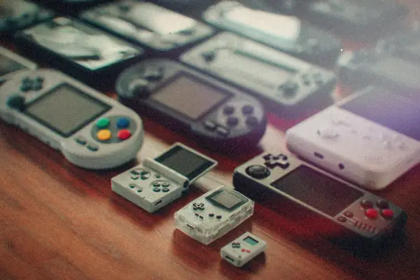 A wooden table covered in retro-style emulation handhelds of different shapes and sizes, from tiny keychain units to wide-screen models.