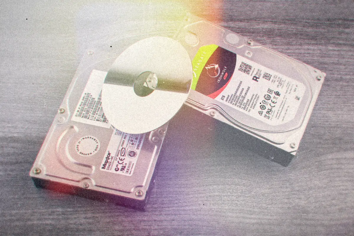 Two computer hard drives and a shiny disc lying on a wooden surface.