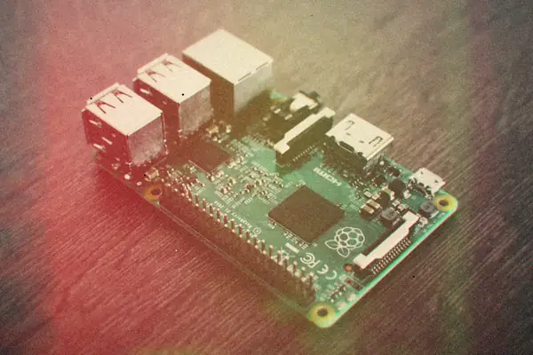 A bare Raspberry Pi board with its USB, Ethernet and HDMI ports on a dark wooden table.