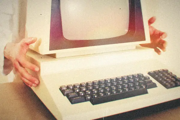 Hands lifting a vintage computer with a CRT monitor and chunky keyboard.