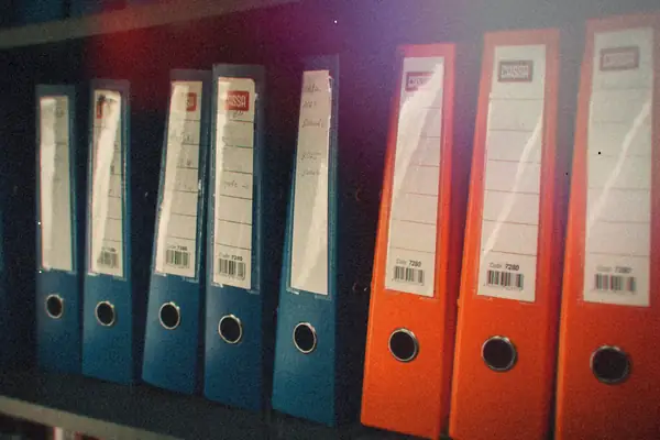 A shelf of blue and orange office binders lined up with labeled spines.