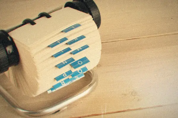 A Rolodex card file with blue alphabet tabs sitting on a pale wooden desk.